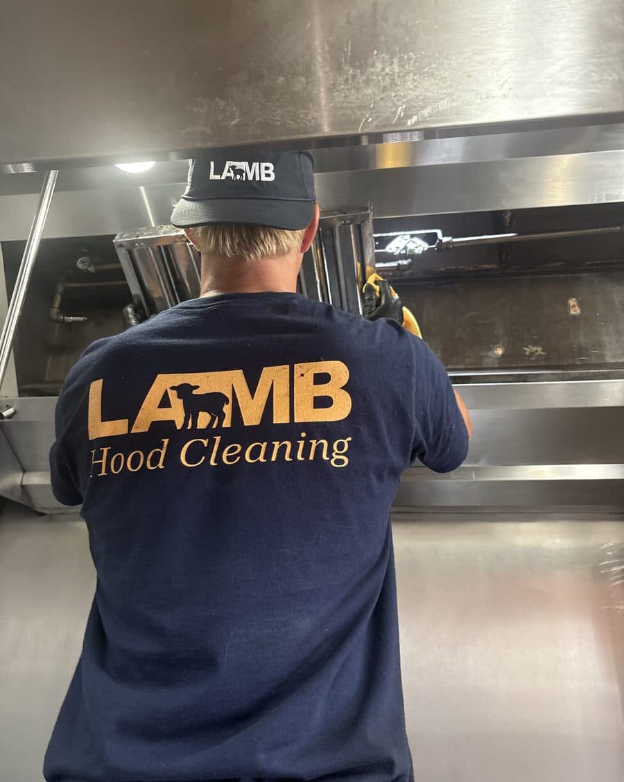 A Lamb Hood Cleaning technician cleaning the interior of a commercial kitchen hood.